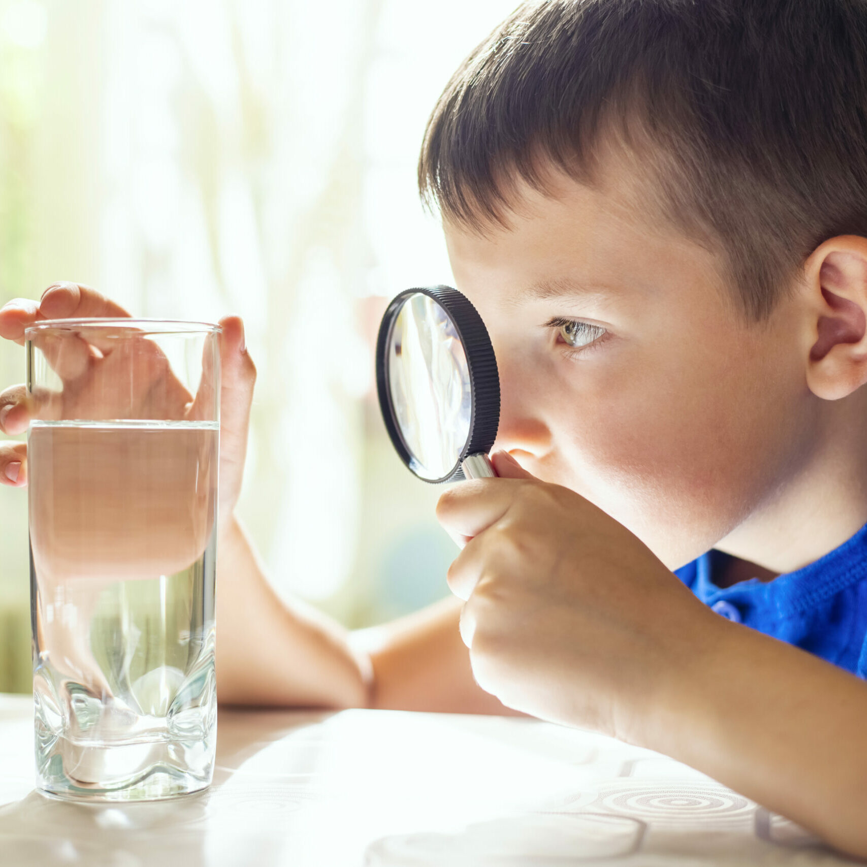 The child boy looking at water in a glass through magnifying glass